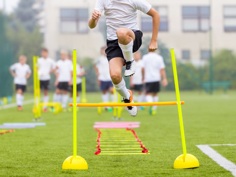 Football field equipment with a player jumping over a hurdle during soccer training drills.