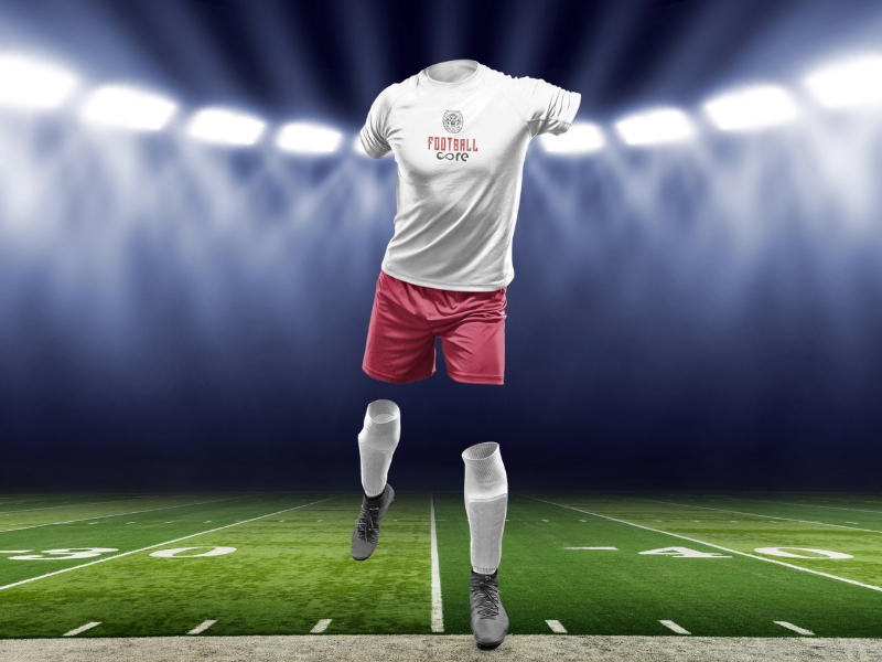 Football apparel on display: white jersey, red shorts, socks, and shoes under stadium lights, highlighting professional gear.