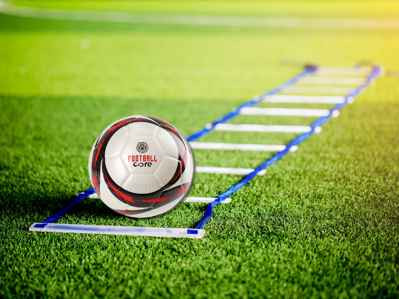 Football field equipment including an agility ladder and a soccer ball placed on the grass.