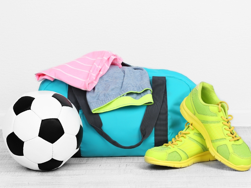 a football bag with clothes on the top shoes in the side and a ball