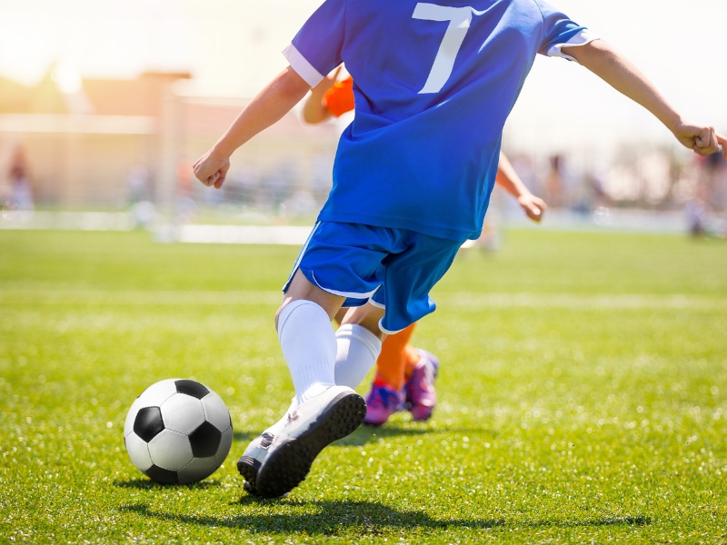 Player wearing a football team jersey with number 7, skillfully dribbling a soccer ball on the field.