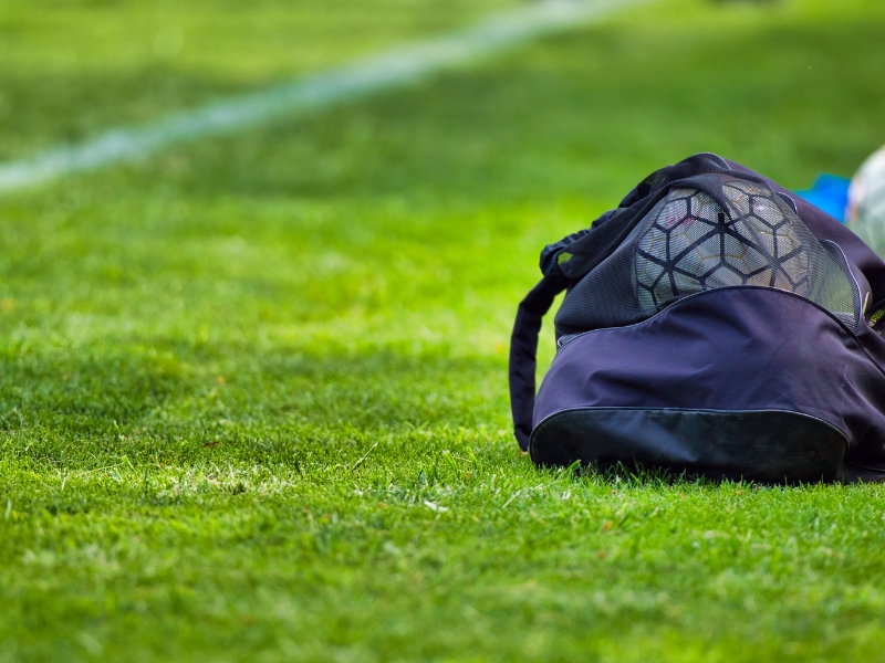 a foot ball gear bag in the side of the field with a ball inside