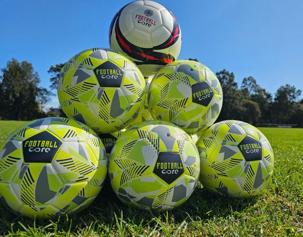 A variety of soccer balls neatly displayed on a vibrant green field, showcasing a bulk buy option for footballs.